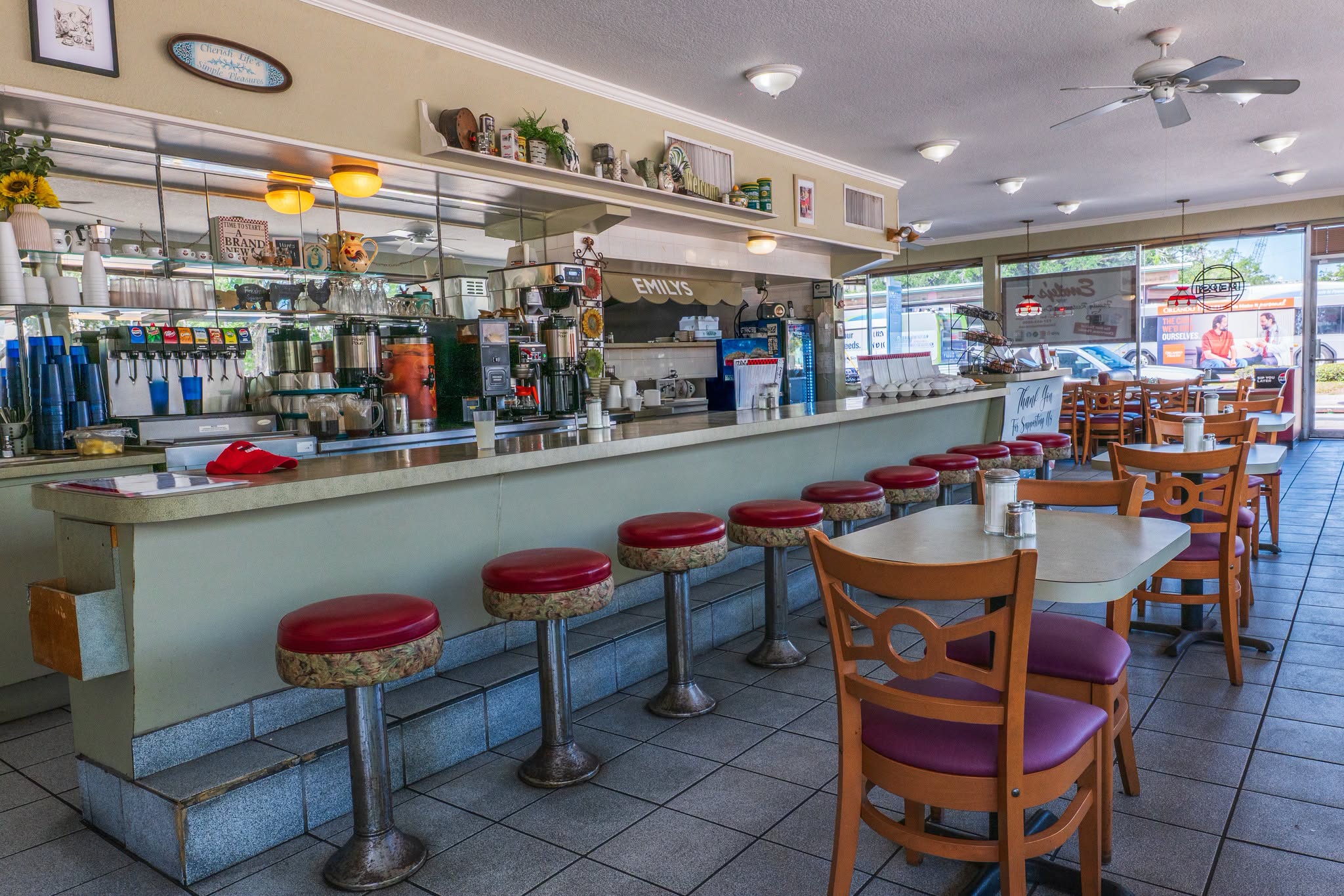 Interior of Emily’s Restaurant featuring counter seating with red stools, dining tables and the open service area.